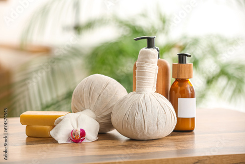 Herbal massage bags, bottles of cosmetic products and soap bars on wooden table