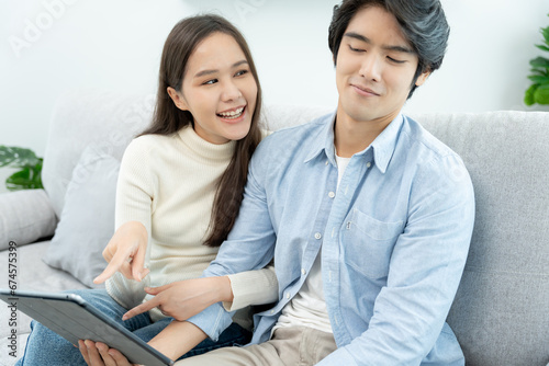 Asian couple smiling and happily use smartphone to online shopping. Husband ready to pay birthday present for beautiful wife. Find accommodation online for honeymoon, App online, book flight tickets. © Shisu_ka