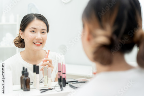 Beautiful Asian woman sit in front of a mirror and smile on makeup. face of a healthy woman applying makeup. Advertisement  lifestyle   cosmetics  makeup accessories  beauty activity  beautician