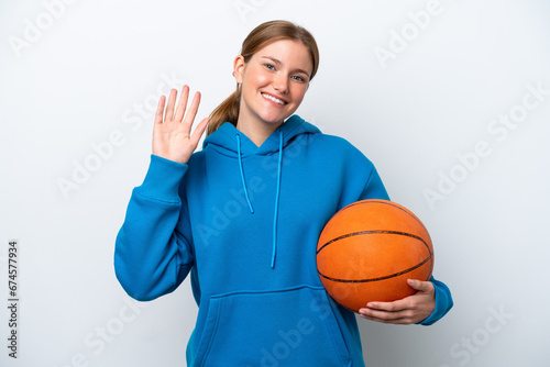 Young caucasian woman playing basketball isolated on white background saluting with hand with happy expression © luismolinero