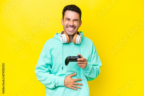 Young handsome man playing with a video game controller over isolated wall smiling a lot © luismolinero