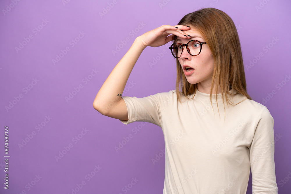 Young English woman isolated on purple background doing surprise gesture while looking to the side Young English woman isolated on purple background doing surprise gesture while looking to the side