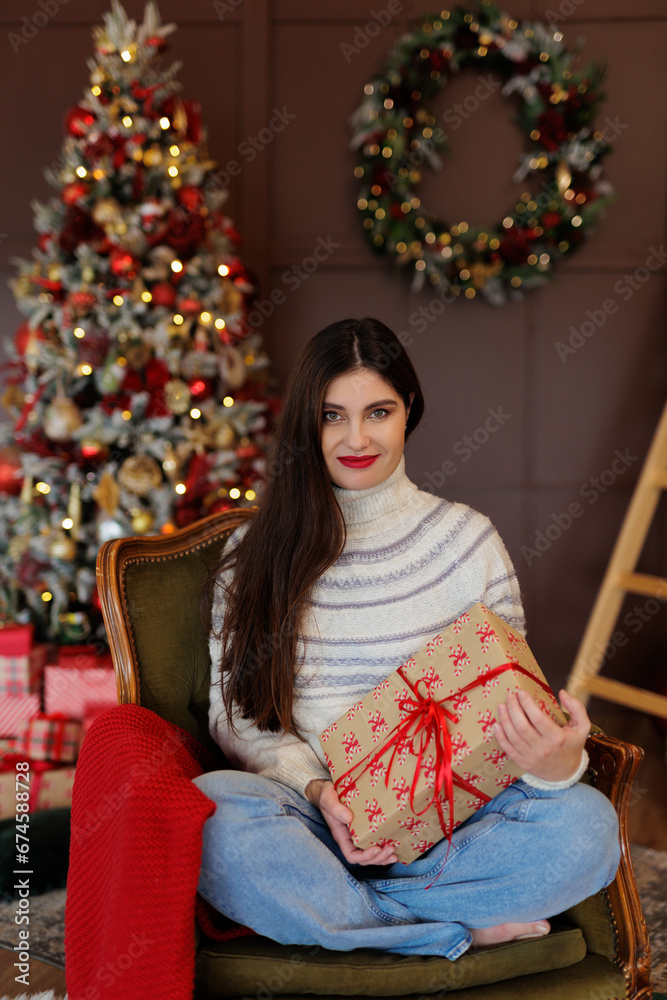 Woman in jeans and sweater sitiing on armchair with red gift