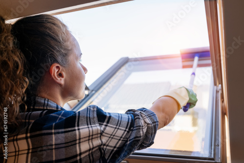 Brunette woman cleaning roof light window at home using squeegee. photo
