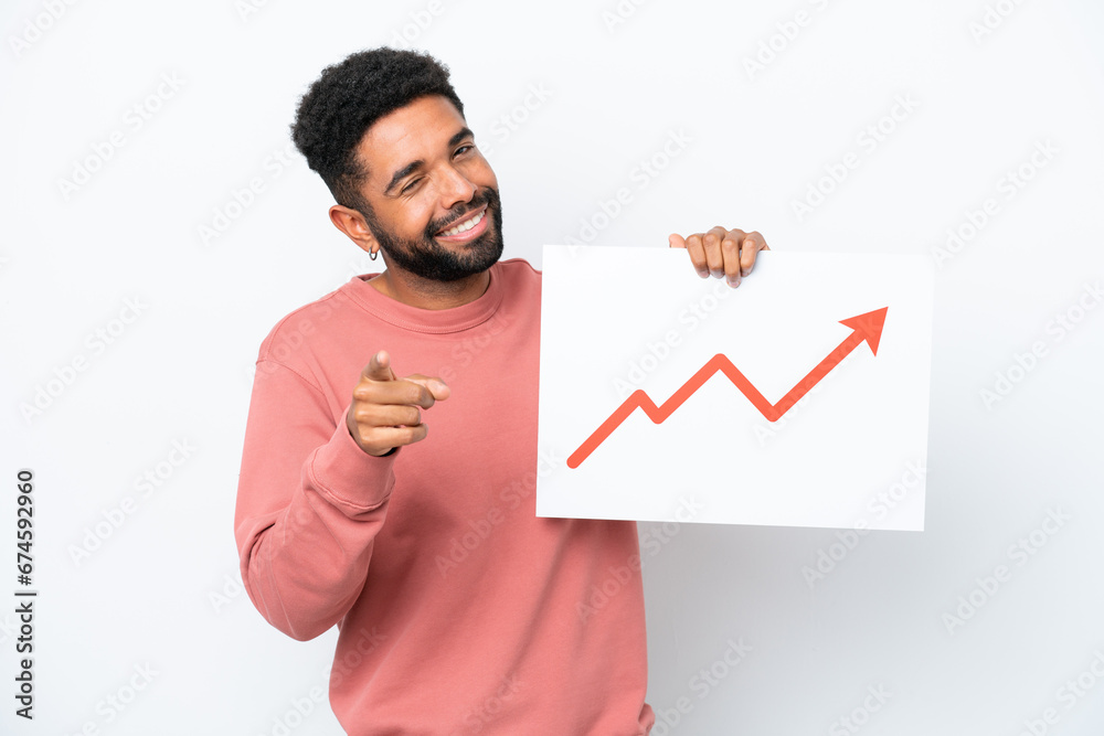 Young Brazilian man isolated on white background holding a sign with a growing statistics arrow symbol and pointing to the front Young Brazilian man isolated on white background holding a sign with a growing statistics arrow symbol and pointing to the front