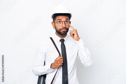 Young architect Brazilian man with helmet and holding blueprints isolated on white background having doubts and thinking