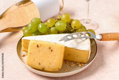 Plate with tasty cheese and grapes on white background
