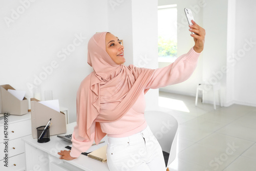 Mature Muslim woman with mobile phone taking selfie at home