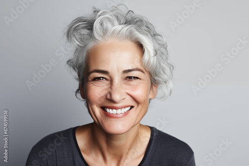 Radiant Mature Woman with Gray Hair Smiling Happily against a Plain Gray Background photo