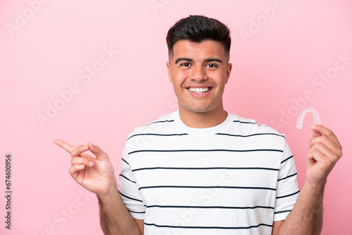Young caucasian man holding invisaling isolated on pink background surprised and pointing finger to the side photo