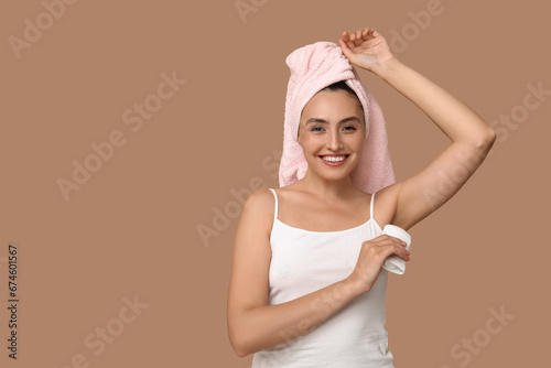 Young woman with deodorant on brown background