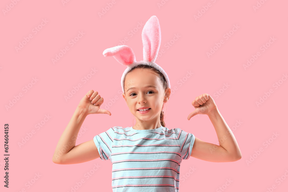 Little girl in bunny ears showing dislike on pink background Little girl in bunny ears showing dislike on pink background