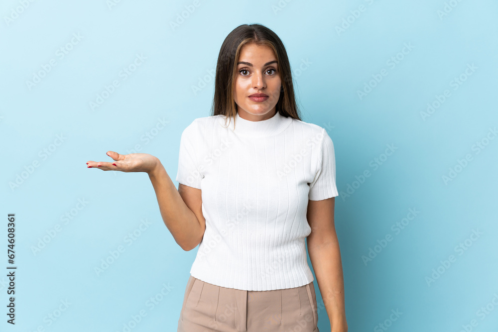 Young Uruguayan woman isolated on blue background making doubts gesture