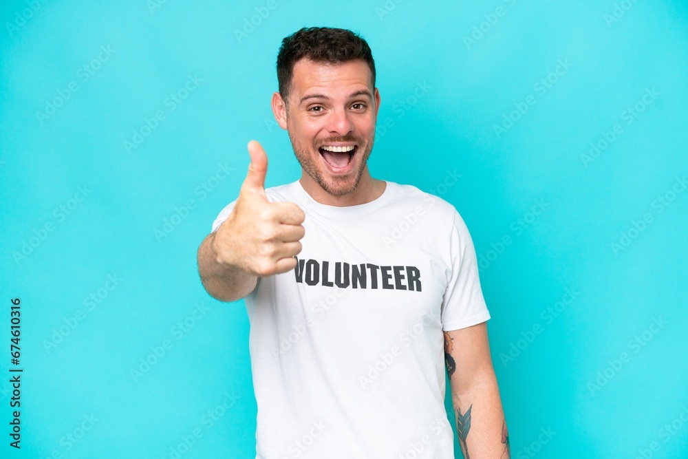 Young volunteer caucasian man isolated on blue background with thumbs up because something good has happened Young volunteer caucasian man isolated on blue background with thumbs up because something good has happened