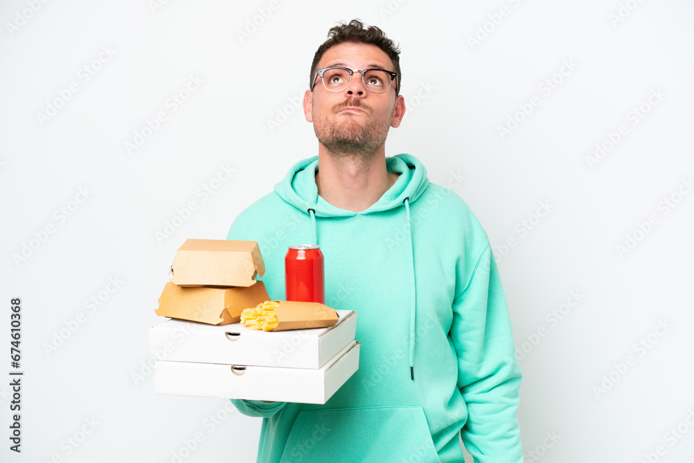 Young caucasian man holding fast food isolated on white background and looking up Young caucasian man holding fast food isolated on white background and looking up