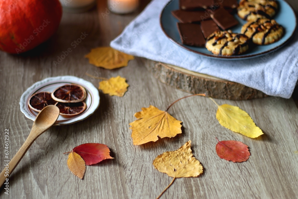 Cup of tea or coffee, plate with desserts, dried oranges, bowl of grapes, scented candles, vintage books, pumpkins and autumn leaves on the table. Autumnal hygge. Selective focus. Cup of tea or coffee, plate with desserts, dried oranges, bowl of grapes, scented candles, vintage books, pumpkins and autumn leaves on the table. Autumnal hygge. Selective focus.