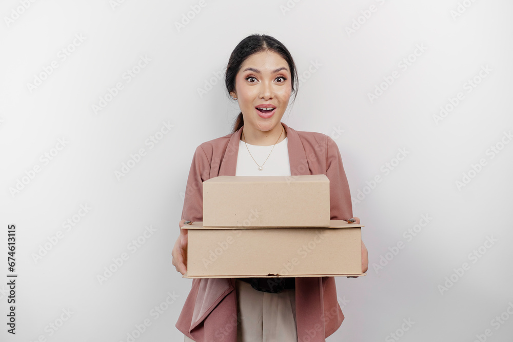 Surprised young Asian woman employee wearing cardigan while holding stack of cardboard boxes, isolated by white background