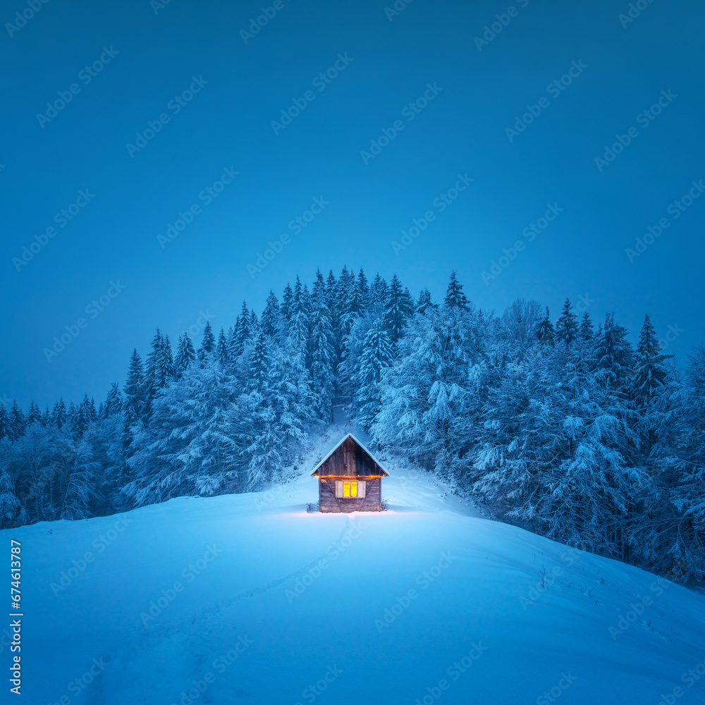 A winter scene with a solitary wooden cabin and snow-covered fir trees in the midst of a forested mountain meadow. Christmas postcard. Snowy mountains forest - obrazy, fototapety, plakaty 