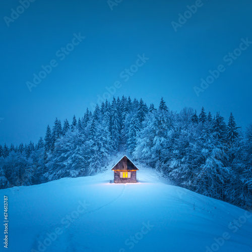 A winter scene with a solitary wooden cabin and snow-covered fir trees in the midst of a forested mountain meadow. Christmas postcard. Snowy mountains forest