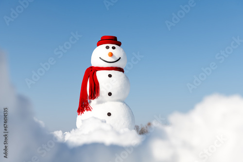 A cheerful snowman donning a fashionable red hat and matching scarf stands proudly in a snowy field, set against a clear blue sky. Christmas postcard © Ivan Kmit