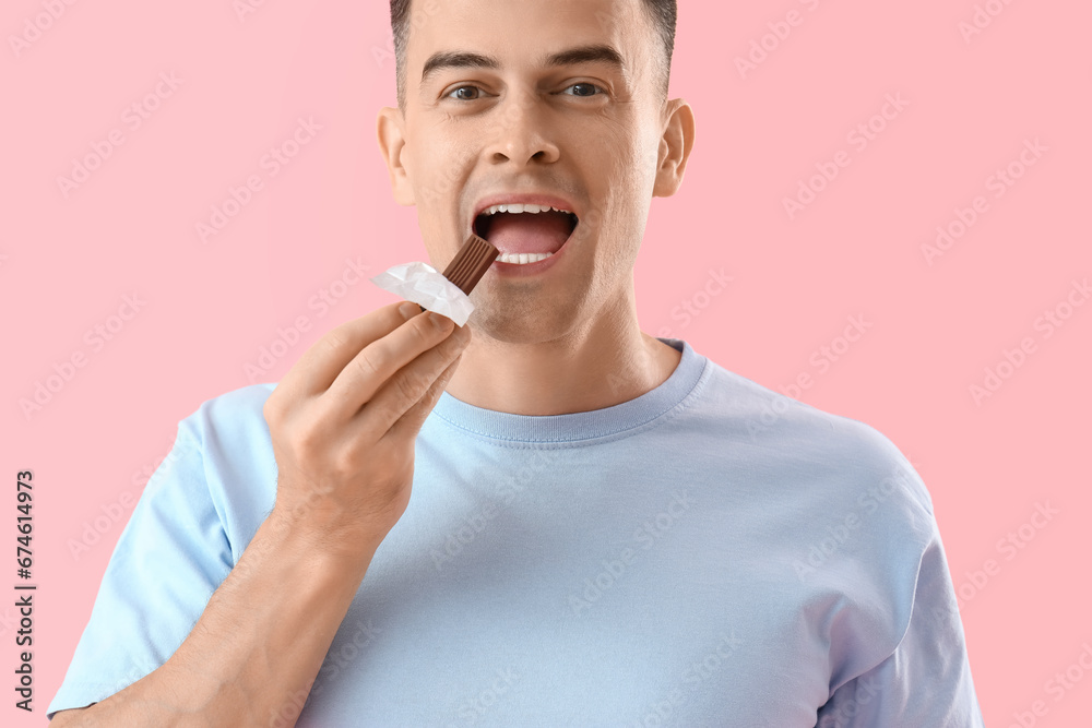 Handsome man eating chocolate on pink background, closeup Handsome man eating chocolate on pink background, closeup