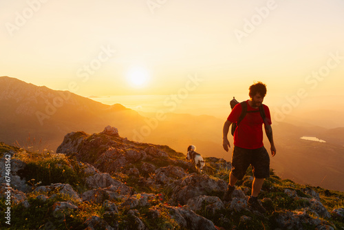 young man goes hiking with his dog in the mountains at sunset. trekking and adventure. sport with pet