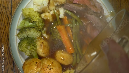 Closeup overhead shot of steaming gravy being poured from a measuring jug over a dinner plate of traditional roast beef, vegetables and Yorkshire pudding. photo