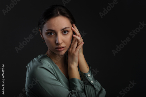 Portrait of a dark-eyed beautiful woman dressed in a green blouse, she has gold earrings and looks at camera against dark gray background, copy space