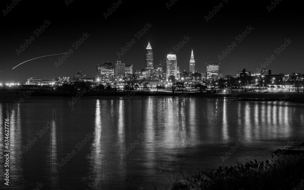Black and White Photo of City Lights Reflecting in the Water with Airplane Light Trail