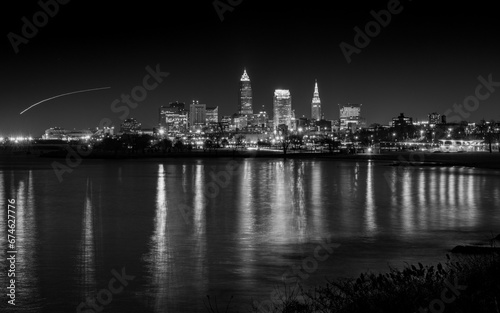 Black and White Photo of City Lights Reflecting in the Water with Airplane Light Trail