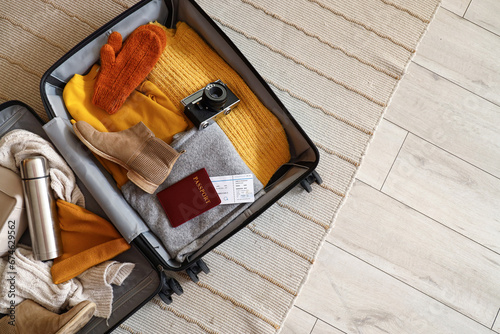 Open suitcase with travelling accessories and winter clothes on carpet, top view photo