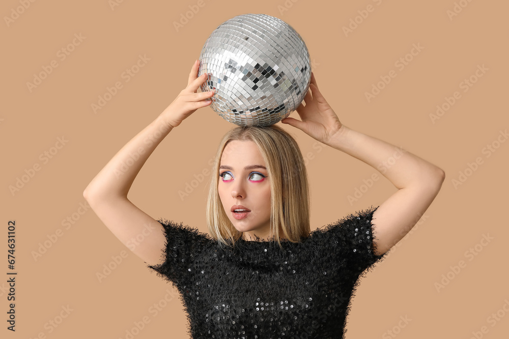 Naklejka premium Beautiful thoughtful young woman with disco ball on brown background
