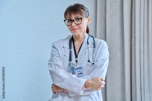 Portrait of mature female doctor looking at camera with arms crossed in office