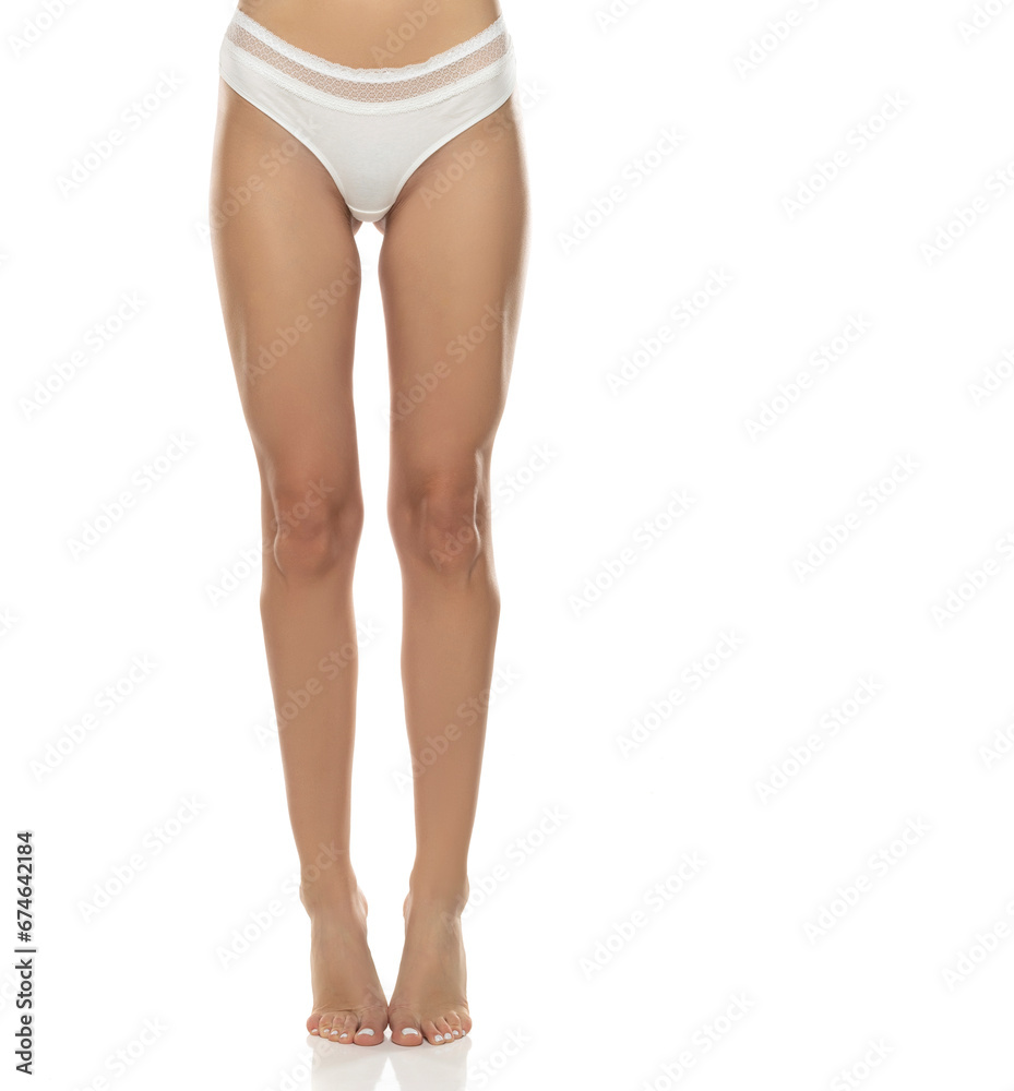 woman's legs are elegantly posed, showcasing white panties from the front on white background.Femininity, sensuality, and body positivity