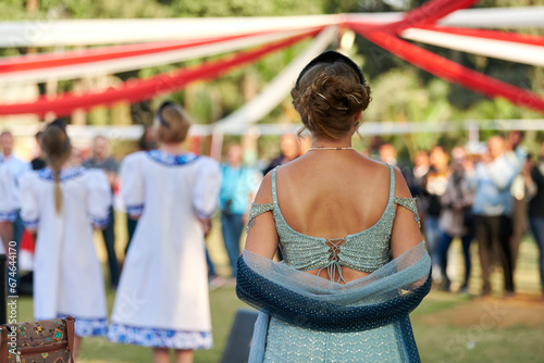Back view of attractive woman in backless green dress looks at dancing performance at festival photo