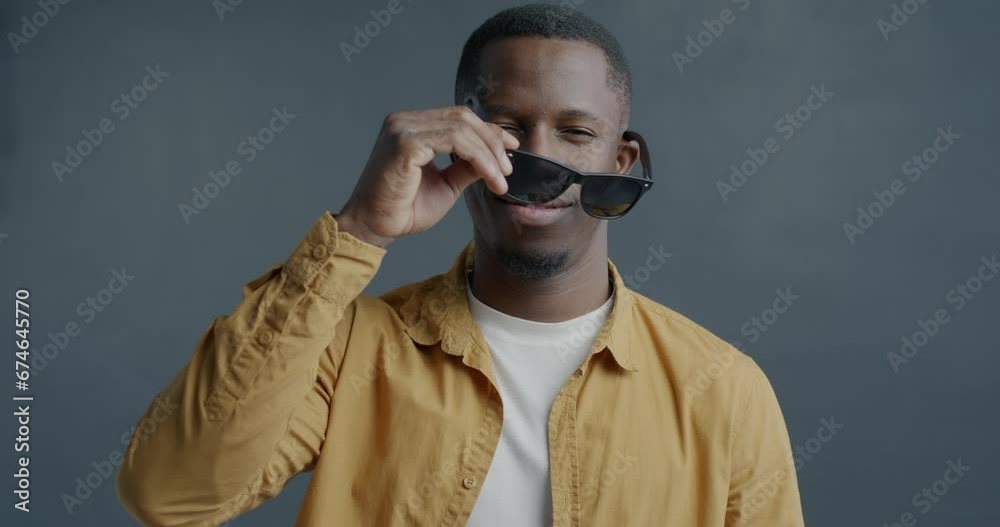 Slow motion portrait of charming African American man taking off sunglasses making eyes flirting on gray background. People and emotion concept. Slow motion portrait of charming African American man taking off sunglasses making eyes flirting on gray background. People and emotion concept.