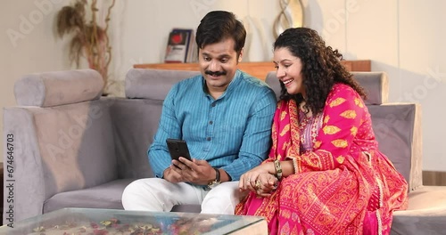Happy Married Couple Spend Time Sitting On Sofa At Home Shopping Online on Mobile Phone
