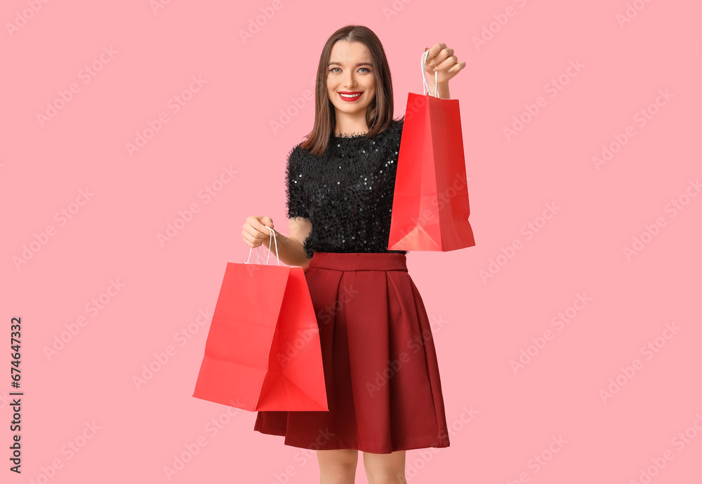 Young woman holding shopping bags on pink background