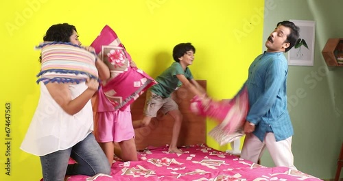 Parents and kids playing with pillow or  having fun in a bedroom
