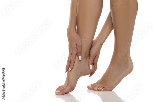 Woman is gently massaging and applying lotion to her bare feet, promoting self-care, relaxation, and foot skincare. Clopse up on a white stdio background photo