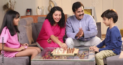 Siblings playing chess while their parents watching them
