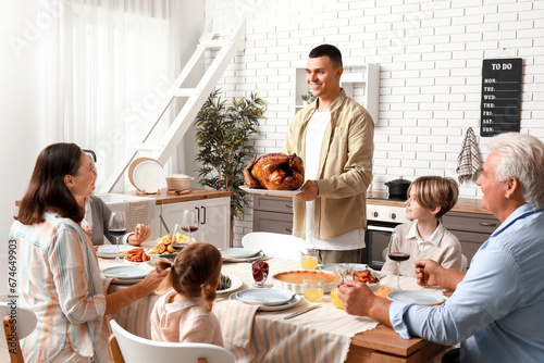 Young man bringing turkey at festive table with his family on Thanksgiving Day