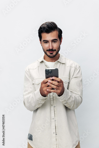 Close-up portrait man holding a phone smile typing a message, chatting online freelance work on a white isolated background, fashionable clothing style, copy space, space for text © SHOTPRIME STUDIO