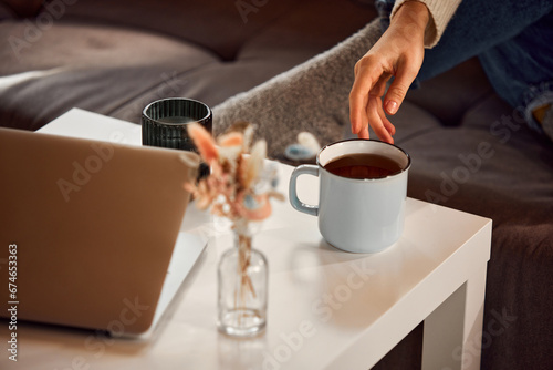 Woman's delicate hand reaches for cup of hot fragrant tea standing on coffee table at home. Relaxing atmosphere. concept of lifestyle, winter holiday season, autumn weekend, relax and cozy.