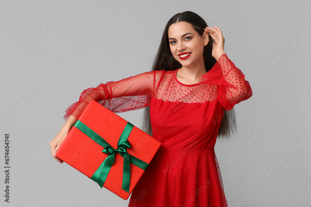Beautiful young woman with Christmas gift on grey background Beautiful young woman with Christmas gift on grey background