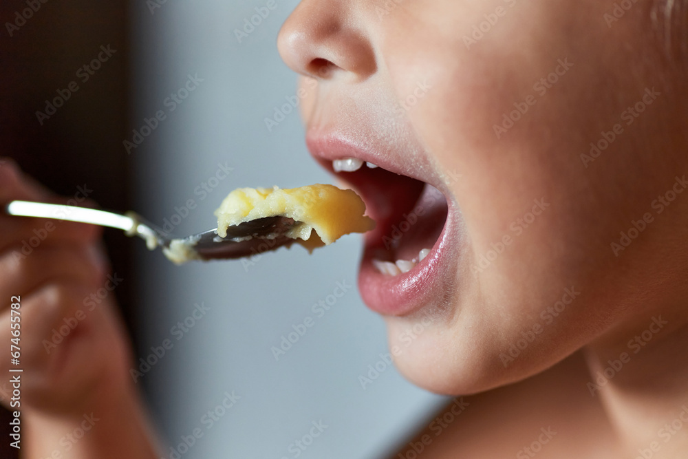 Close-up: a child's mouth with a spoon of mashed potatoes held up to it. Three-quarter turn. Close-up: a child's mouth with a spoon of mashed potatoes held up to it. Three-quarter turn.