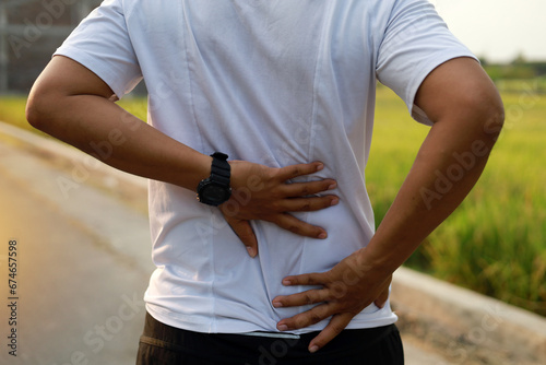 Close up photo of Asian Man with back pain during doing outdoor exercise.