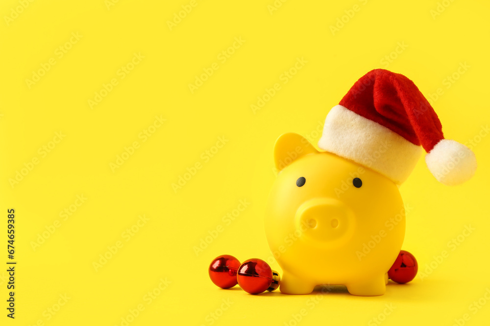 Piggy bank with Santa hat and Christmas balls on yellow background Piggy bank with Santa hat and Christmas balls on yellow background