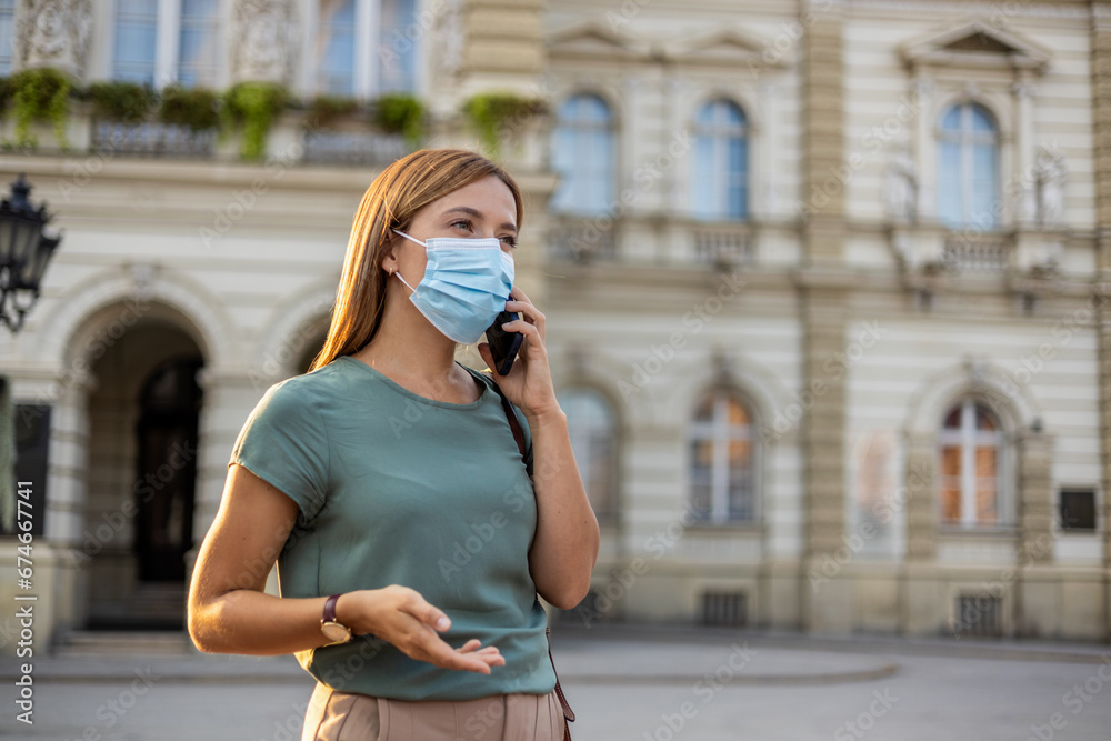Beautiful woman with blue face mask using smart phone on the street. Young attractive caucasian woman with a protective face mask and a smart phone in her hand.