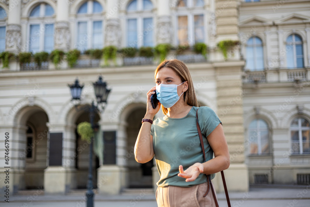 Portrait of young business woman office worker in medical protective mask talking on cellphone outdoor, city street background. Epidemic, pandemic, healthcare, people and business concept.